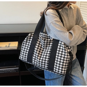 Close-up of a large houndstooth travel bag with durable black handles and shoulder strap