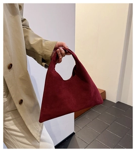 Detail of burgundy suede tote bag held by model wearing a beige trench coat