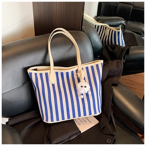 Detail of blue striped canvas tote with beige leather handles and white plush charm on sofa