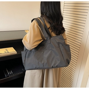 Detail of checkered canvas tote bag with side pocket shown on a model's shoulder