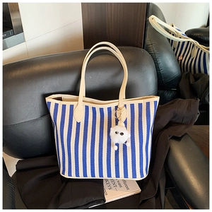 Close-up of blue and white striped canvas tote with cream handles and white plush charm