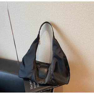 Detail of a black nylon hobo bag featuring a leather buckle and gold zipper on a book