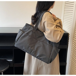 Detailed side view of a large plaid tote bag worn by a model in a cozy interior