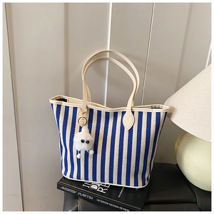 Detail of blue and white striped canvas tote bag featuring a cute white plush monster charm