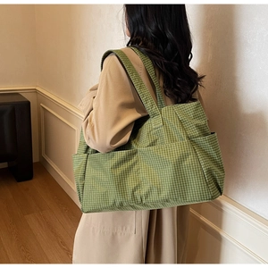 Detail of green checkered canvas tote bag showing side pocket and long shoulder strap