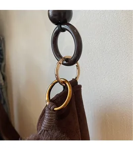 Detail of the brown suede tote bag featuring a gold metal ring and resin link attachment