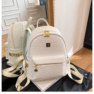 Detailed close-up of tweed backpack texture with gold zippers and metal logo plate