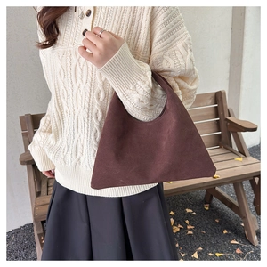 Detail of a dark brown suede tote bag carried by a model in a knit sweater