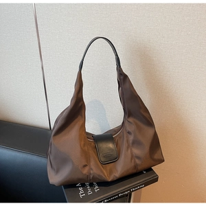 Detail of dark brown nylon hobo bag with leather flap on black leather sofa