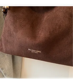 Close-up of deep brown suede tote bag with decorative wooden beads and gold logo detail