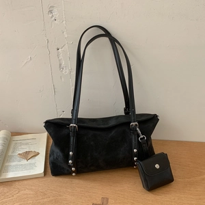 Detail of black matte tote bag with rivet accents and matching mini pouch on wooden desk