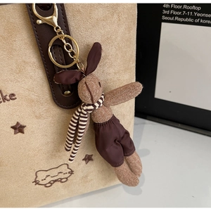 Close-up of beige suede tote bag featuring cat embroidery and a cute rabbit plush charm
