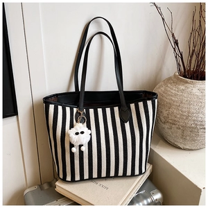 Detail of striped canvas tote with black leather handles and fluffy charm on a vintage case