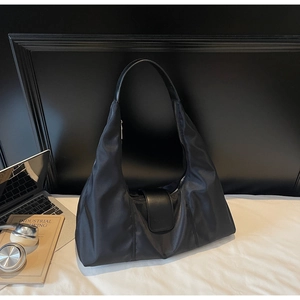 Close-up of large black nylon hobo bag with laptop and lifestyle items on white linens