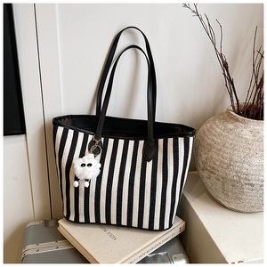 Detail of striped canvas tote bag featuring slender shoulder straps and a plush charm