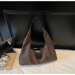 Detail of dark brown nylon hobo bag with leather trim and metal clasp on white bedding