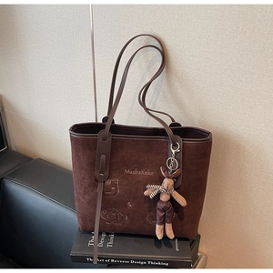 Close-up of brown suede tote bag with cartoon cat embroidery and plush bunny charm