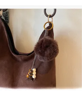 Detail of faux fur pom-pom and wooden bead keychain hanging on a brown suede tote bag