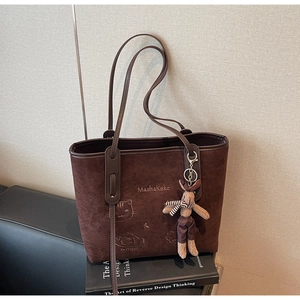 Detail of a brown suede tote bag featuring cat embroidery on a book in a stylish scene
