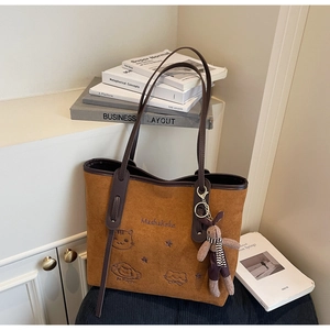 Close-up of brown suede tote bag with custom cat embroidery and plush rabbit pendant