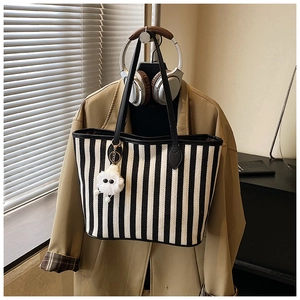 Detailed close-up of striped canvas tote bag with plush charm and leather trim details