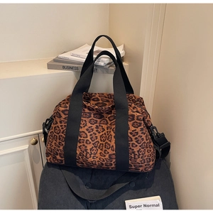 Detail shot of leopard print travel bag with black adjustable strap on corduroy chair