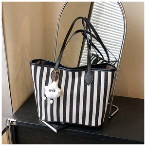 Detailed view of striped canvas tote bag with black leather straps and plush sheep charm