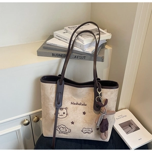 Detail of beige suede tote bag with cartoon cat embroidery and bunny charm on white cabinet