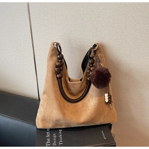 Détail de la poignée en perles de bois et du pompon marron sur un sac en daim de chameau