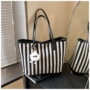 Close-up of black and white striped canvas tote bag with a white furry monster charm