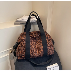 Detail of canvas travel bag with leopard print pattern and black woven straps on a stool