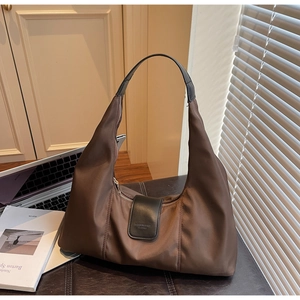 Detail of deep brown nylon tote bag with leather handles on a black leather bench