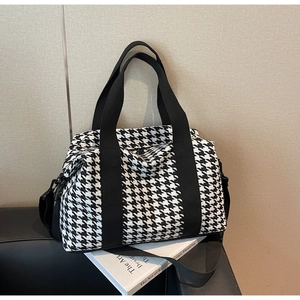 Close-up of houndstooth travel bag with black straps on a sofa, showing fabric texture