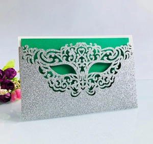 Detail of laser cut silver glitter mask invitation with green inner card and floral accent