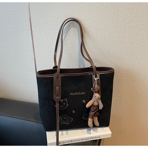 Detail of black suede tote bag with embroidery, brown leather trim, and a bunny charm