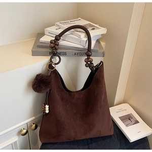 Détail du sac à bandoulière en suède avec poignée en perles de bois et pompon décoratif
