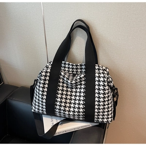 Detail of classic black and white houndstooth travel tote bag on a black leather sofa