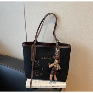 Detail of black suede tote bag with embroidery, leather handles and bunny charm accessory