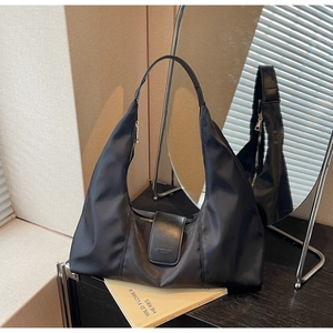 Detail of black nylon hobo bag featuring magnetic leather flap with text logo