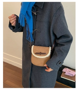 Sacoche en daim marron avec bordure en laine, portée sur un manteau gris et une écharpe bleue