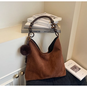Détail du sac hobo en similicuir marron avec des perles en bois et un pompon pelucheux