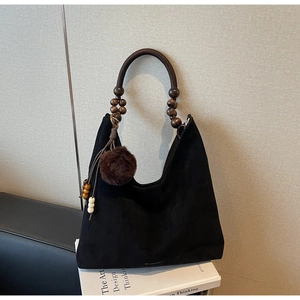 Détail du sac cabas en suédine noire avec poignée en perles de bois et pompon en fourrure