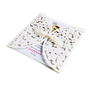 Detail of laser-cut floral invitation with butterfly motifs and a cream satin ribbon bow