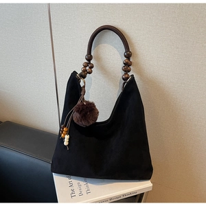 Détail d'un sac hobo en daim noir avec poignée en perles de bois et breloque à pompon