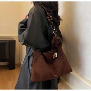 Détail d'un cabas en daim marron avec bandoulière en perles de bois et pompon doux