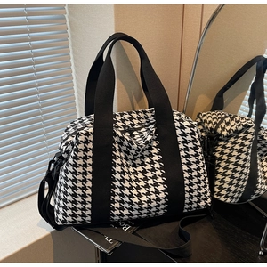 Detail of high-capacity houndstooth travel bag with durable black straps and zipper