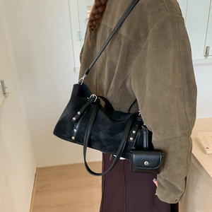 Detail of black suede tote with silver studs worn with an olive leather jacket