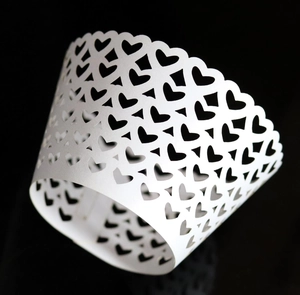 Close-up of white laser-cut cupcake wrapper with hollow heart patterns for party decor