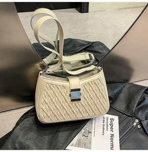 Close-up of cream quilted crossbody bag with silver buckle on a black leather jacket