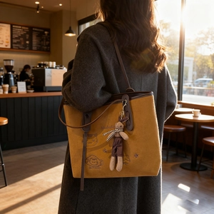 Brown leather tote bag with cat embroidery and rabbit charm shown in warm cafe lighting